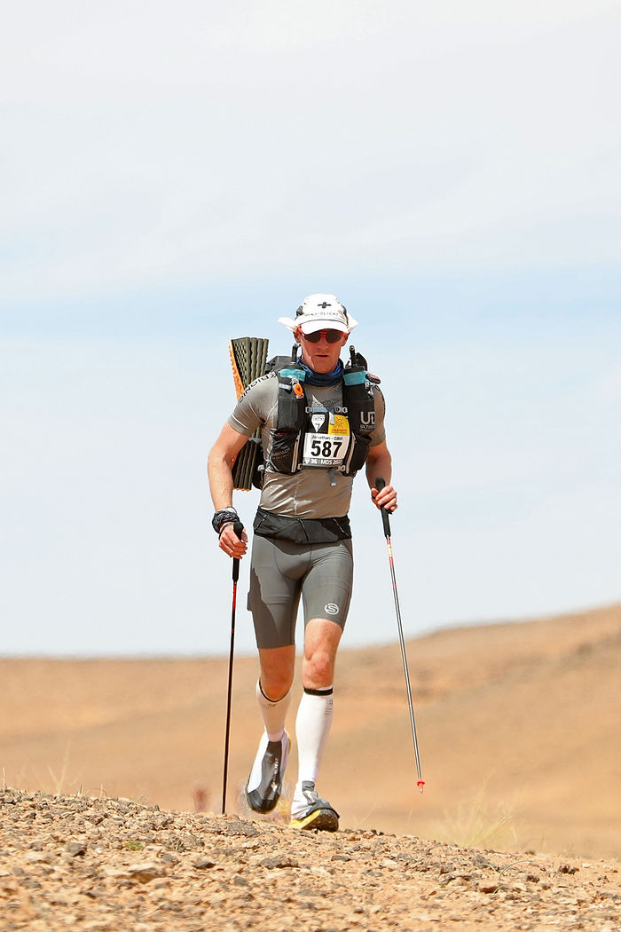 athlete running in the Sahara with poles and backpack marathon des sables